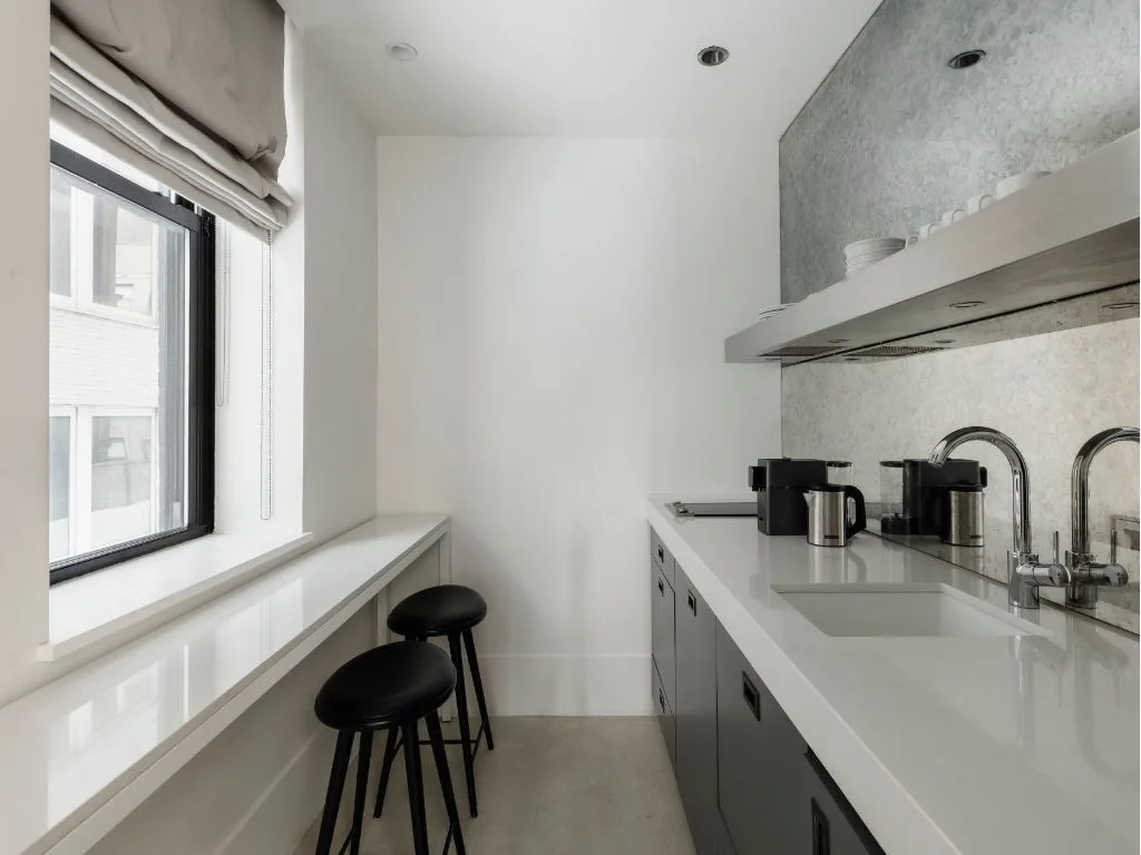 A modern kitchen with white countertops and black stools.