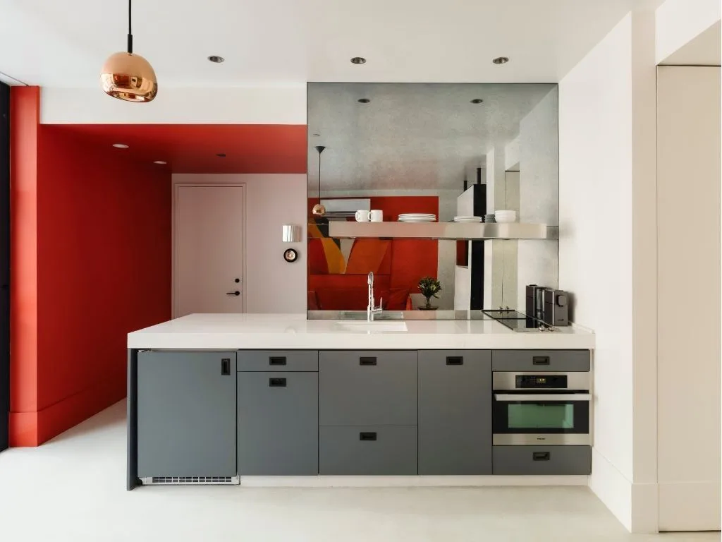 Modern kitchen with red and white walls, gray cabinets, and a copper pendant light.