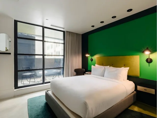 Une chambre d'hôtel avec un lit, un mur vert et une grande fenêtre.